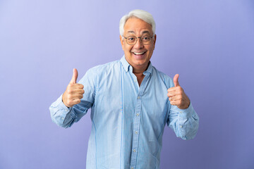 Middle age Brazilian man isolated on purple background giving a thumbs up gesture
