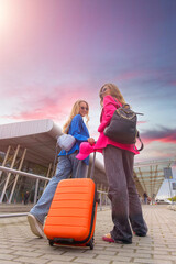 Two happy girls walking near airport, with luggage. Air travel, summer holiday