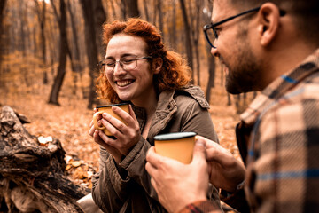 Young couple with backpack drinking tea after hiking in forest.