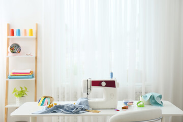 Modern sewing machine, fabric and accessories on table indoors