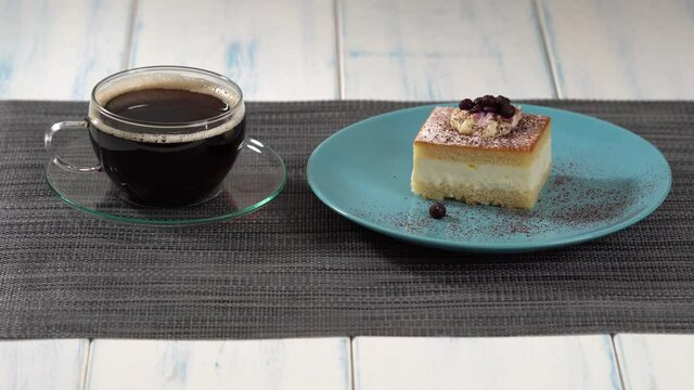 A piece of cake and a cup of coffee on the light wooden table.