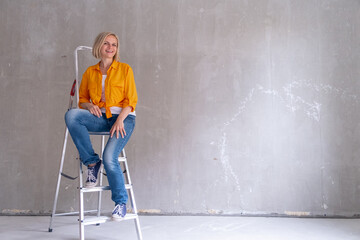 Renovation apartment. happy woman sits on stairs near empty wall at home. Free wall, repairs house...