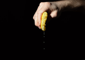 lemon with leaking juice squeezed in hand of man on black background. squeezed like lemon