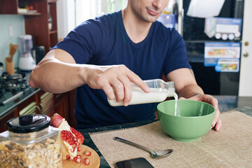 Close-up image of man sitting at kitchen counter and pouring milk in bowl of muesli