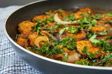 Closeup on sweet and sour chicken patties in a pan on a plaid towel, ready to be served. Chicken cutlets cooked with Asian flavored sauce, onions, and parsley. Chinese style dish, selective focus.