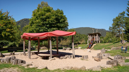 Spielplatz im Park mit einer textilen Überdachung auf Holzpfählen im sandigen Spielbereich