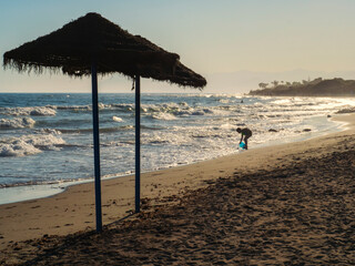 Silueta de un noño jugando con un cubo en la orilla de la playa al atardecer
