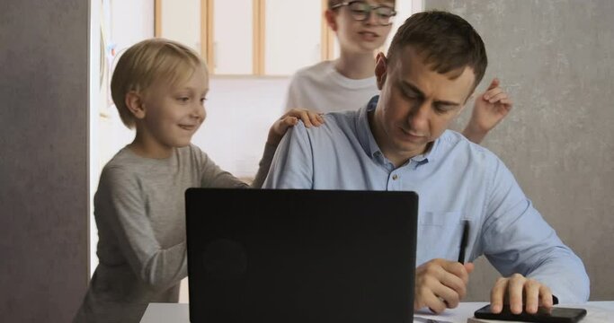 Children distract dad from work. Young male freelancer trying to work at home with two children.