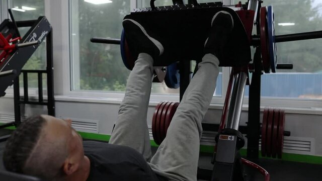 A man in sportswear, with tattoos, his hair partially shaved off, does a platform press with his legs.