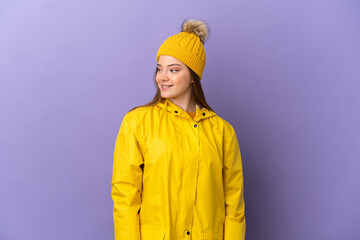 Teenager girl wearing a rainproof coat over isolated purple background looking to the side and smiling