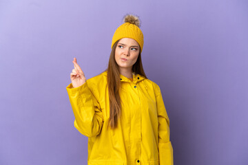 Teenager girl wearing a rainproof coat over isolated purple background with fingers crossing and wishing the best