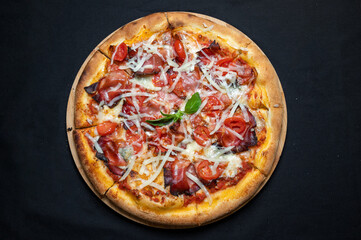 Pizza with tomato sauce, smoked pork ham, chery tomatoes and gorgonzola cheese on a black background