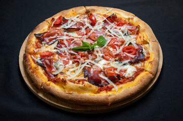 Pizza with tomato sauce, smoked pork ham, chery tomatoes and gorgonzola cheese on a black background