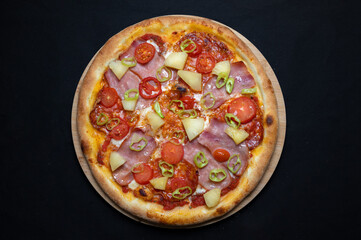 Pizza with tomato sauce, chicken ham, spicy salami, cherry tomatoes, pineapple and hot peppers on a black background
