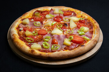 Pizza with tomato sauce, chicken ham, spicy salami, cherry tomatoes, pineapple and hot peppers on a black background