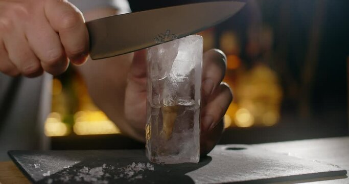 Bartender makes crushed ice from large ice cube by sharp knife, making the cocktail on the bar counter, refreshing cold drinks, 4k Prores HQ 120fps