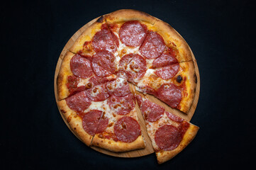 Pizza with tomato sauce, mozzarella and salami on a black background.