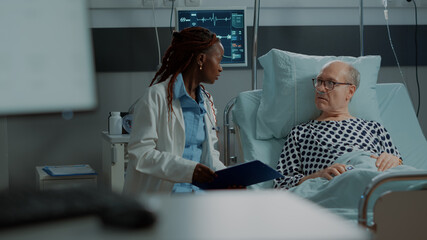 Multi ethnic medical staff explaining disease to patient in hospital ward bed at clinic. Sick old man with nasal oxygen tube in intensive care room preparing for medicine against health problems