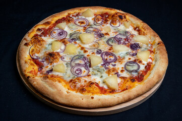 Pizza with tomato sauce, mozzarella, gorgonzola cheese, red onion and pineapple on a black background.