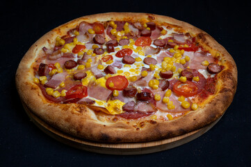 Pizza with tomato sauce, mozzarella, sour cream, salami, pork ham, sausages, corn and cherry tomatoes on a black background