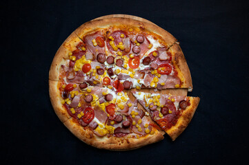 Pizza with tomato sauce, mozzarella, sour cream, salami, pork ham, sausages, corn and cherry tomatoes on a black background