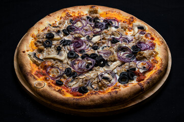 Pizza with tomato sauce, mozzarella, ground tuna, red onion, olives and mushrooms on a black background.