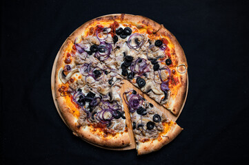 Pizza with tomato sauce, mozzarella, ground tuna, red onion, olives and mushrooms on a black background.