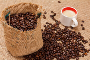Cup of coffee and roasted coffee beans in a canvas sack.