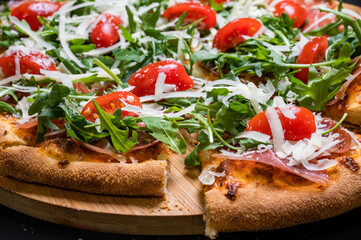 Pizza with tomato sauce, smoked pork muscles, mozzarella, arugula salad and cherry tomatoes on a black background.