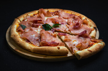 Pizza with tomato sauce, mozzarella and ham on a black background.