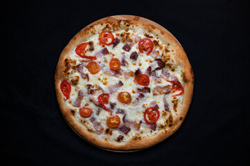 Pizza with tomato sauce, mozzarella, smoked pork ham and cherry tomatoes on a black background.