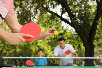 Family with child playing ping pong in park, closeup - obrazy, fototapety, plakaty