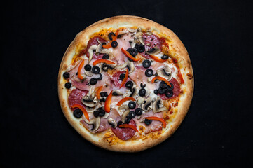 Pizza with tomato sauce, salami, pork ham, olives, peppers and mushrooms on a black background.