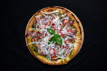 Pizza with tomato sauce, smoked pork ham, avocado sauce, mozzarella and cherry tomatoes on a black background.