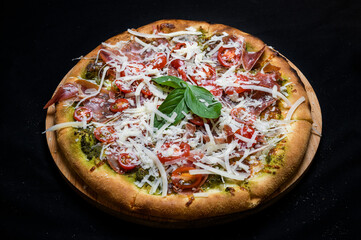 Pizza with tomato sauce, smoked pork ham, avocado sauce, mozzarella and cherry tomatoes on a black background.