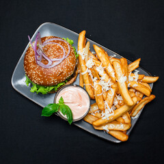 Burger with beef, french fries and sauce on a gray plate