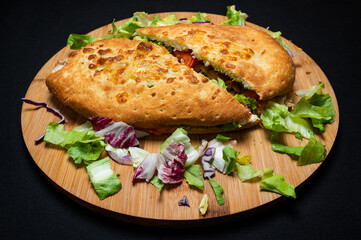sandwich with mozzarella cheese, cedar cheese, mushrooms, red peppers and iceberg lettuce on a wooden plate on a black background.