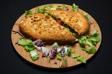 sandwich with mozzarella cheese, cedar cheese, mushrooms, red peppers and iceberg lettuce on a wooden plate on a black background.