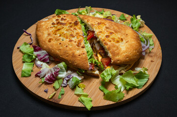 sandwich with mozzarella cheese, cedar cheese, mushrooms, red peppers and iceberg lettuce on a wooden plate on a black background.