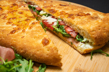 sandwich with smoked pork ham, mozzarella, tomatoes and arugula salad on wooden plate on black background.