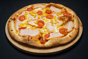 Pizza with tomato sauce, chicken ham, mozzarella, corn and cherry tomatoes on a black background.