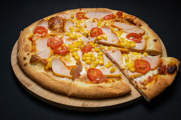 Pizza with tomato sauce, chicken ham, mozzarella, corn and cherry tomatoes on a black background.