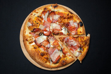 Pizza with tomato sauce, smoked pork ham, mozzarella and cherry tomatoes on black fudal