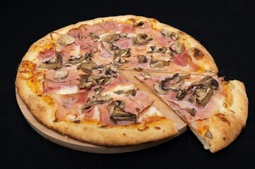 Pizza with tomato sauce, mozzarella, smoked pork ham and mushrooms on a black background.