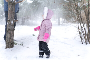 little girl in warm clothes and a fur hood plays hide and seek with dad in the winter forest