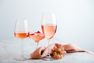 Rose wine in different types of glasses on light grey concrete background with grapes. Rose Wine composition on white table.