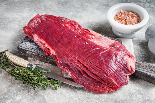 Fresh Flank or flap raw beef steak on wooden board with herbs. Gray background. Top view