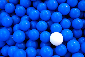 1 white plastic ball, the rest are many blue balls. In the playground used as a background.