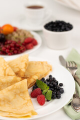 Blurred image on a light background of pancakes in a white plate, decorated with different fruits, a plate with fruits, cutlery.The concept of proper nutrition