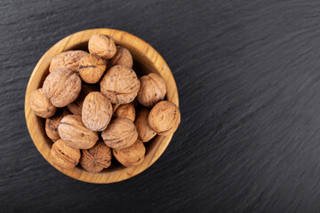 Walnut in wooden bowl on black background with copy space.